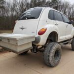 white pt cruiser lifted on a truck frame with a tool box on the back at the gambler 500