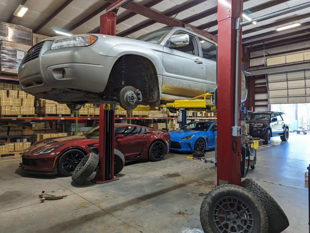 subaru forester on a lift with a burgandy c7 corvette, a blue brz, and a 4 runner in the background.