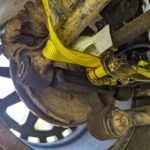 yellow ratchet strap wrapped around damaged suspension parts keeping them together on a 2006 subaru forester