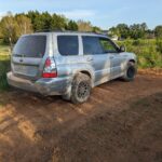 silver subaru forester sg on dirt tires parked on a dirt track in a field